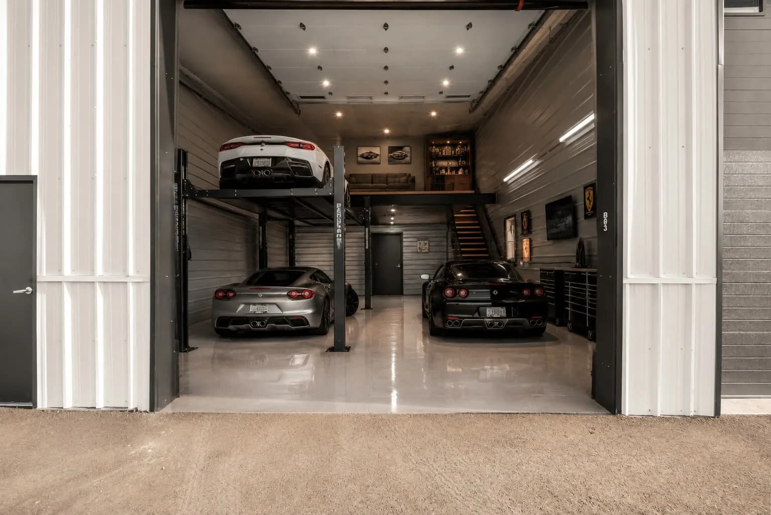 A finished garage bay with supercars on a four-post lift and a loft lounge with a bar